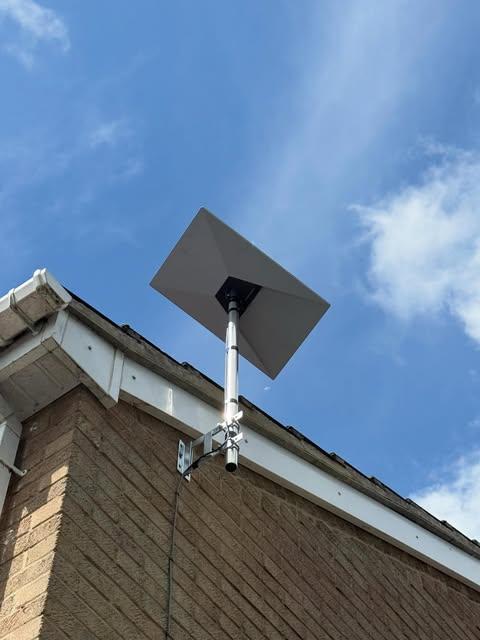 Satellite dish on a pole mount fixed to a residential brick wall under a clear sky