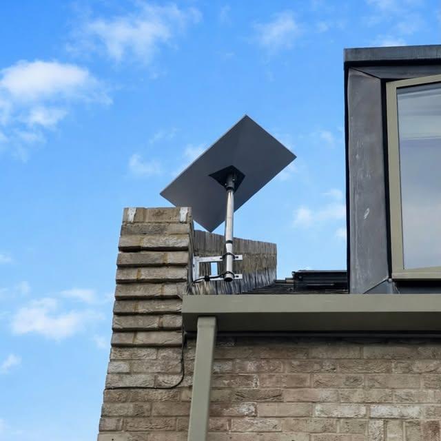 Satellite dish pole-mounted on a brick chimney with clear sky line of sight