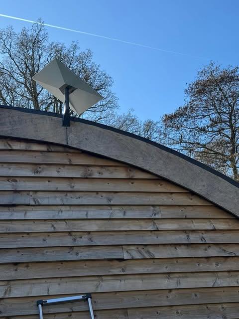 Satellite dish mounted on a curved wood-clad building during a professional install