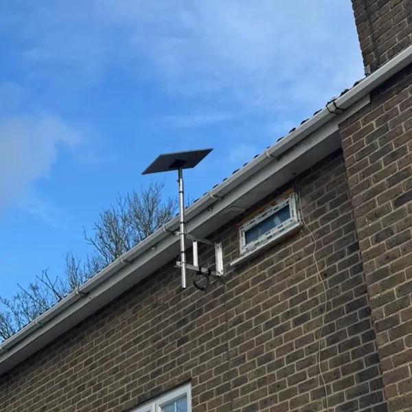 Satellite dish on a wall mounted pole bracket fixed to brown brick with tidy cable management under a clear sky
