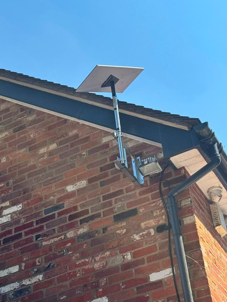 Satellite dish on a tall wall mast clearing the roofline of a two storey brick house