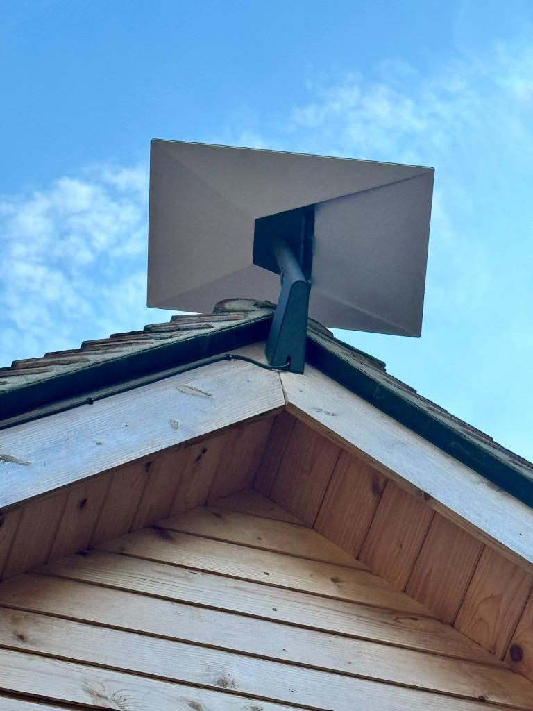 Satellite dish mounted on the wooden eave of a garden office or outbuilding with neat cable clips