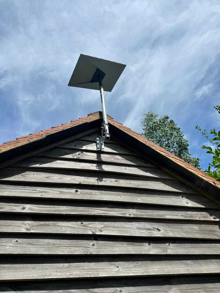 Satellite dish on a tall pole mount fixed to weathered timber cladding for a clear sky view