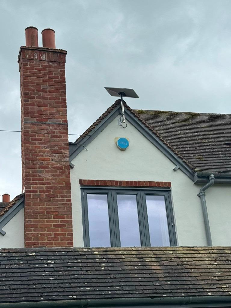 Satellite dish pole mounted on a white rendered gable end beside a brick chimney with tidy cabling