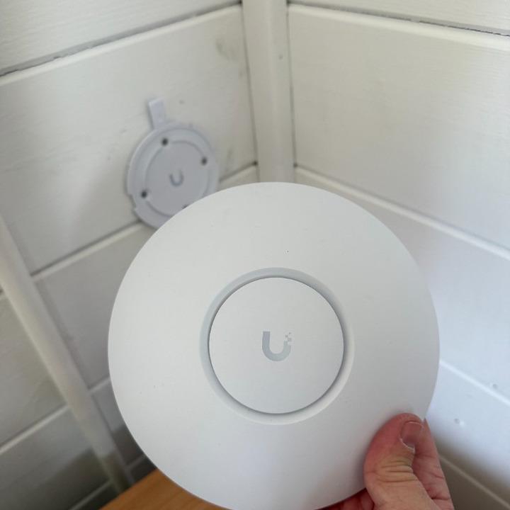 UniFi U7 Lite access point held in front of its wall mount bracket