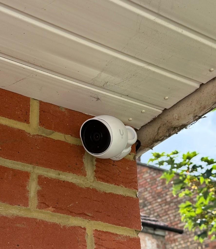 White UniFi G5 Bullet CCTV camera mounted on a red brick wall under the soffit