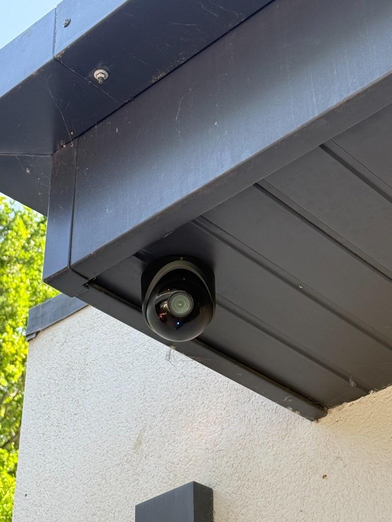 Black UniFi G6 Turret CCTV camera mounted under a dark soffit on a light exterior wall