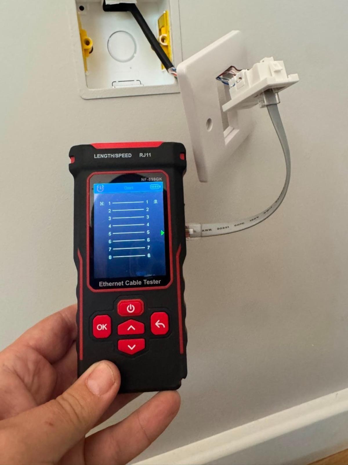 Open wall network socket continuity-checked with a cable tester during a pre-install WiFi survey